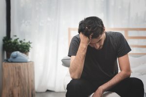 A man sitting on a bed with his head in his hands, depicting depression in daily life.