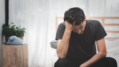 A man sitting on a bed with his head in his hands, depicting depression in daily life.