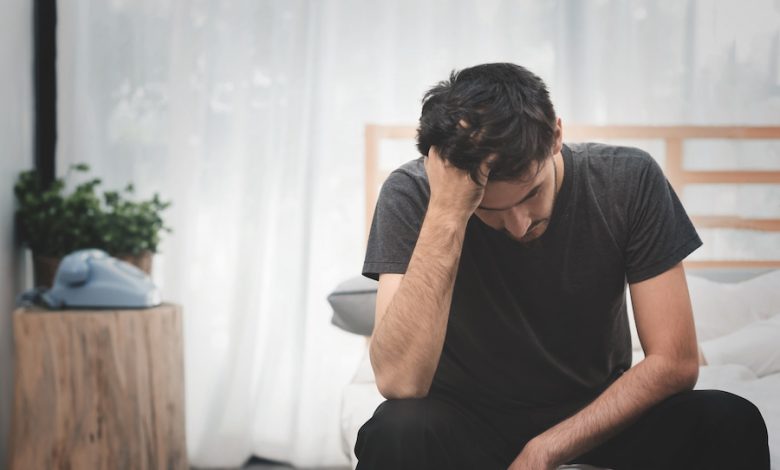 A man sitting on a bed with his head in his hands, depicting depression in daily life.